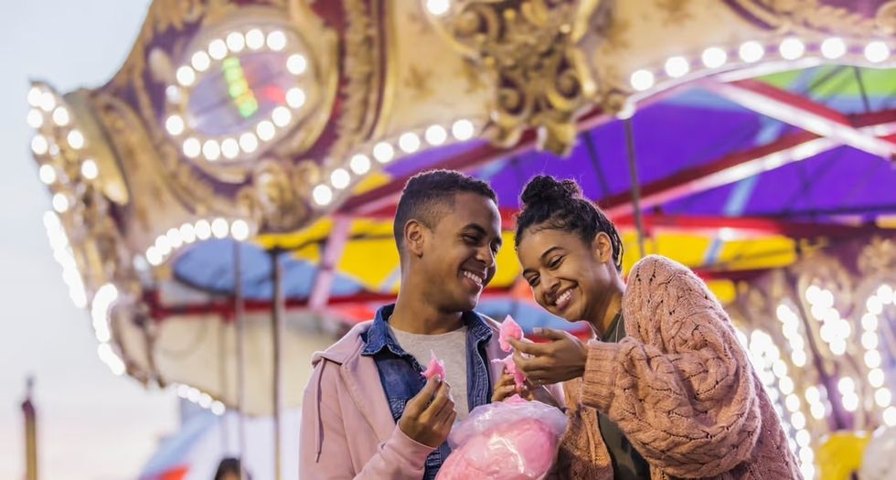Couple smiling and enjoying cotton candy at a brightly lit carousel.