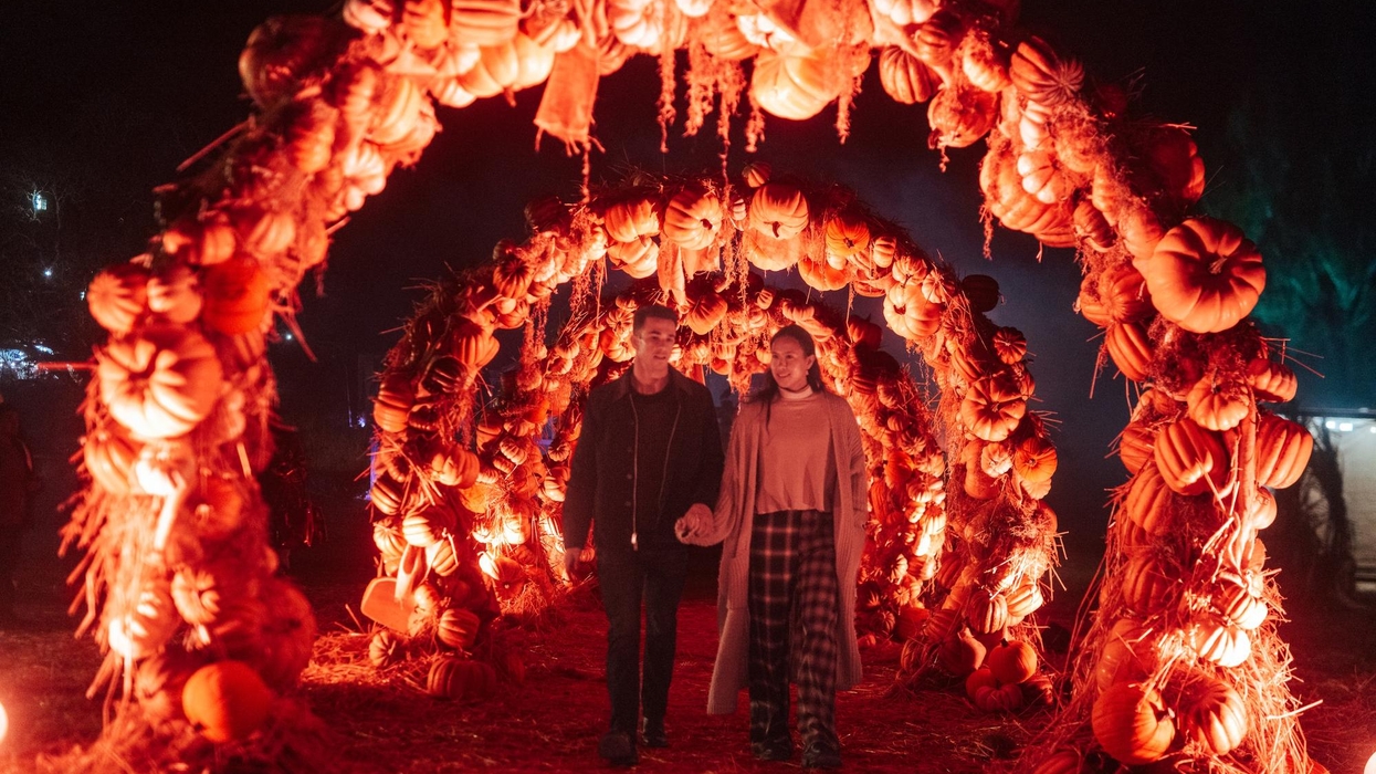 Couple walking through pumpkin arches lit by orange lights at night at Filoli