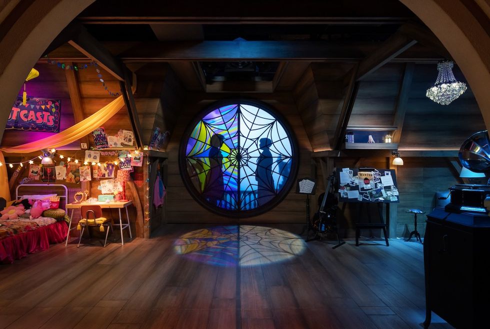 Cozy attic room with stained glass window, craft table, bed, and bulletin board.