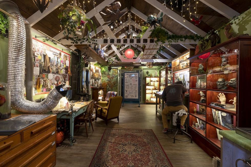 Cozy, cluttered workshop with cabinets, artwork, string lights, and a person working at a desk. W\u0113t\u0101 Workshop Unleashed