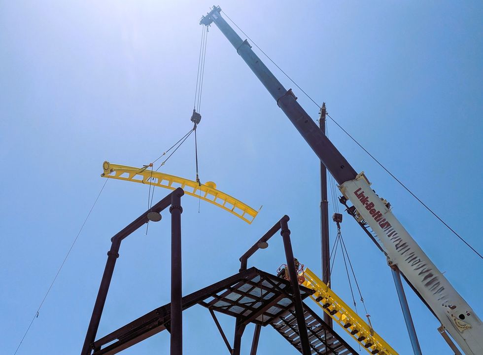 Crane lifting a yellow roller coaster track under a clear blue sky at Oasis at Lake of the Ozarks