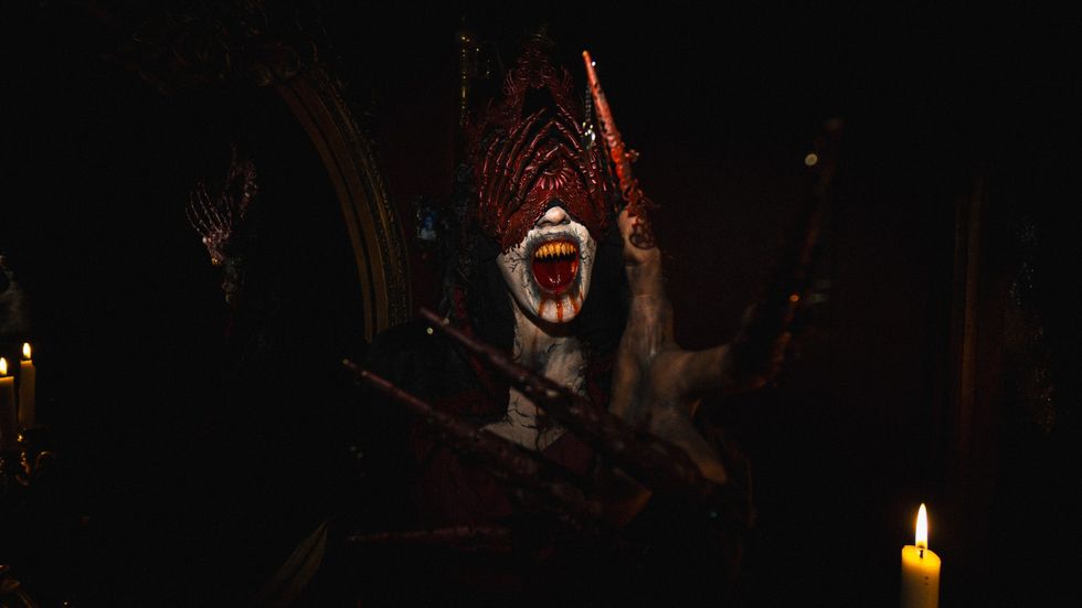Creepy figure with long claws and sharp teeth, surrounded by candles in dim lighting.