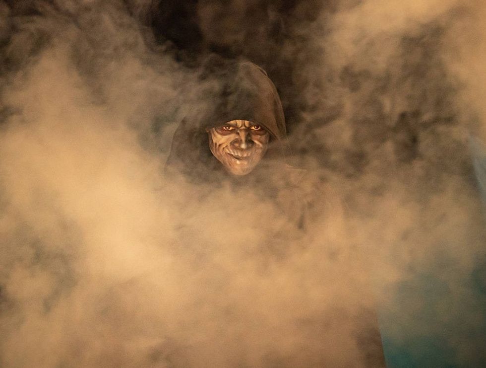 Creepy hooded figure with smoky background and eerie grin.