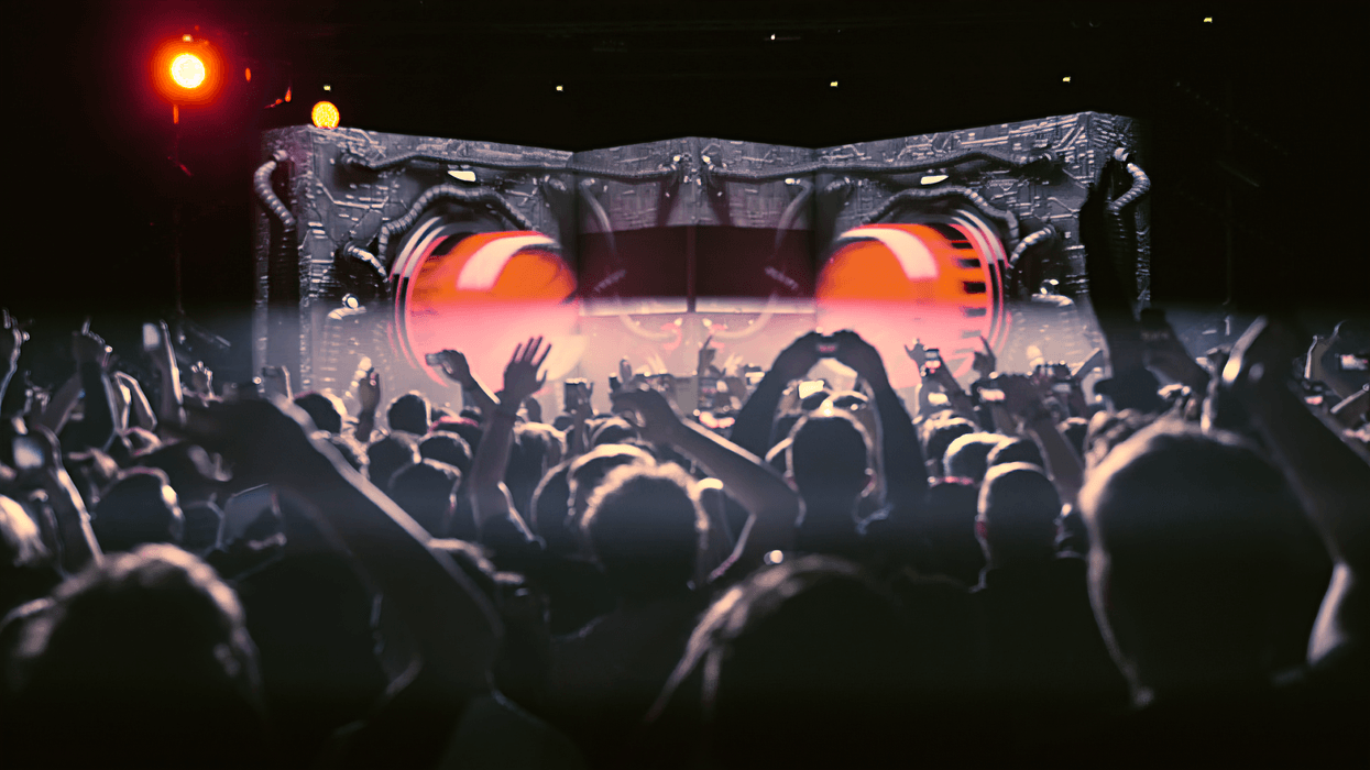 Crowd at a concert with vibrant lights and an industrial-themed stage design.
