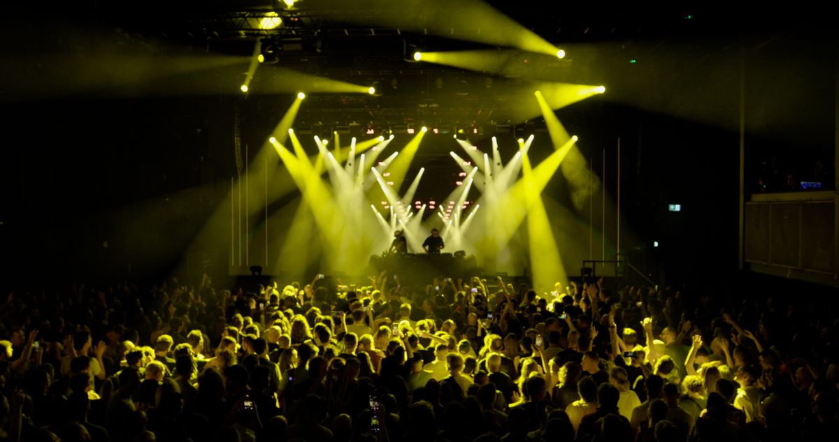 Crowd at a Royksopp concert with a DJ and yellow stage lights, powered by Dimension real-time tech
