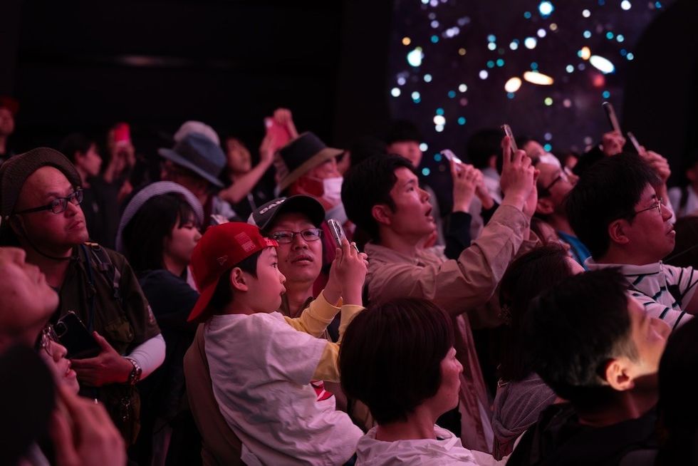 Crowd at USA Pavilion, Expo 2025, gazing up and taking photos, illuminated by colourful lights in a dark setting.