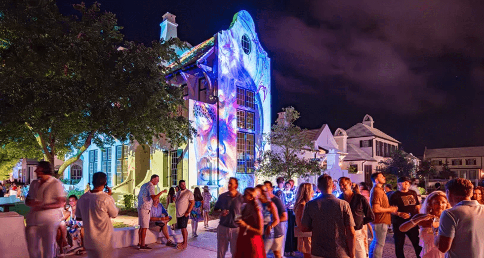 Crowd enjoying outdoor event with colorful projections on a building at night.
