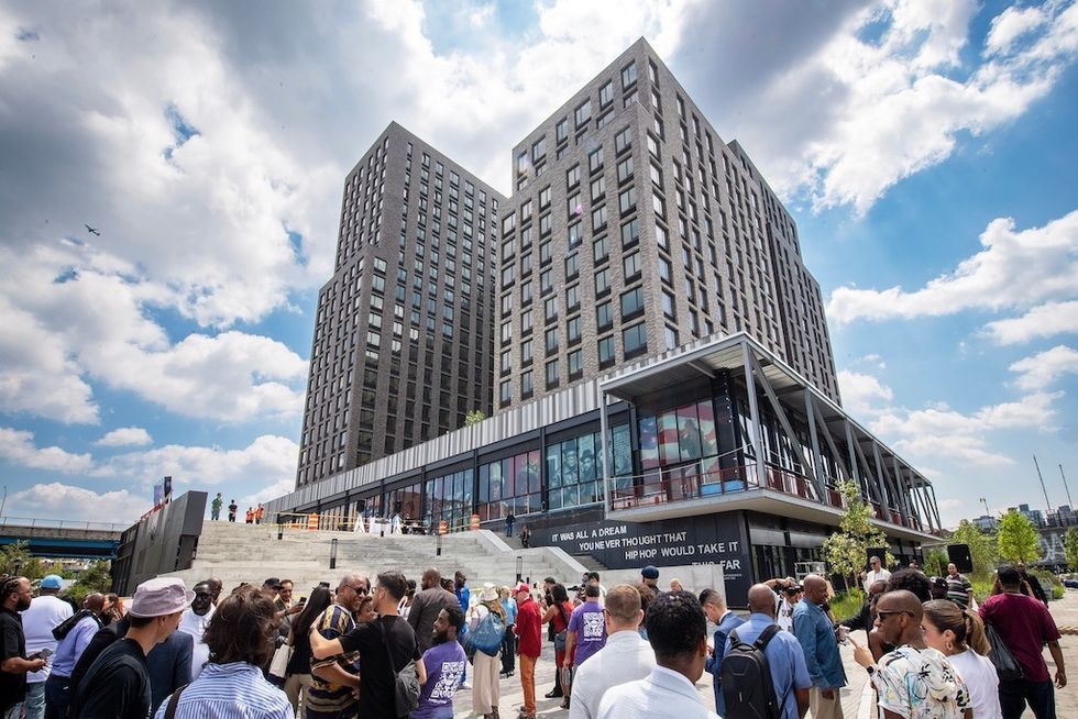 Crowd gathered outside a modern multi-story building, Hip Hop Museum, under a cloudy sky.
