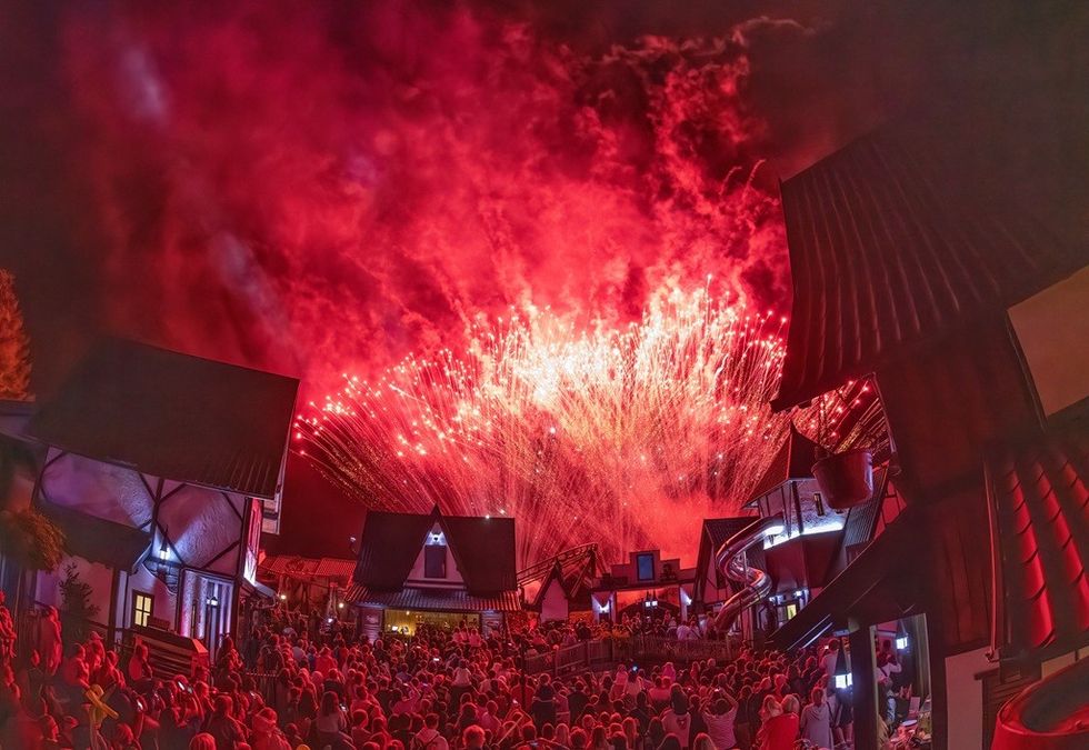 Crowd watching vibrant red fireworks light up the night sky over a village.