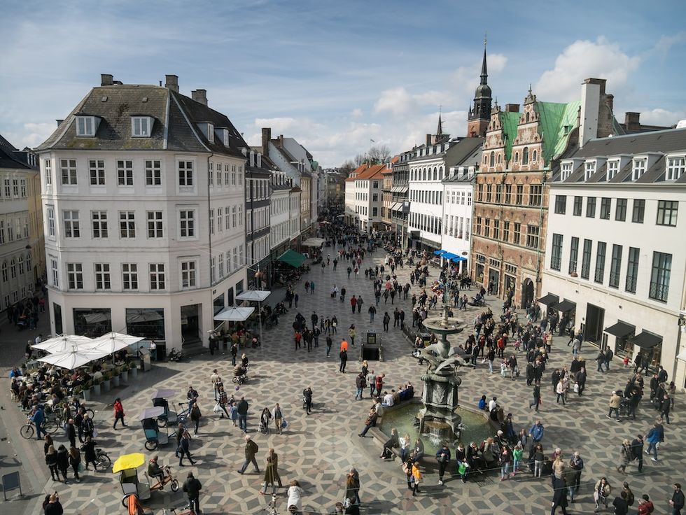Crowded European plaza with historic buildings and a central fountain on a sunny day.