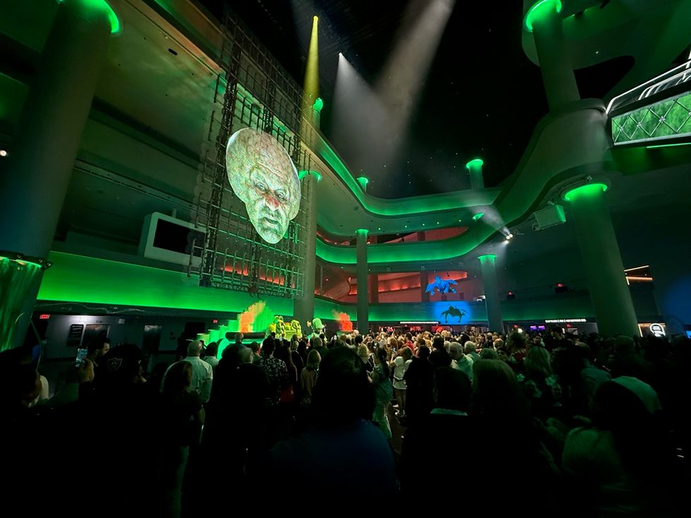 Crowded event space with large, eerie face projection and green lighting.