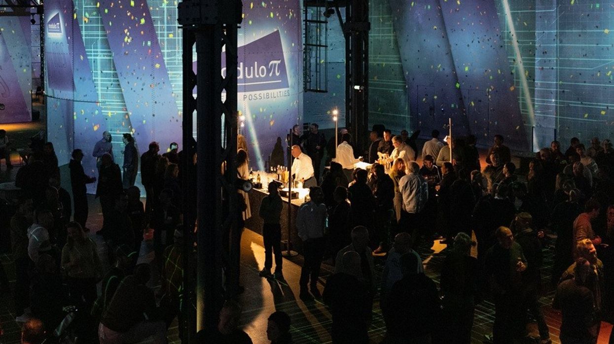 Crowded event with illuminated booths and attendees under colorful lighting.