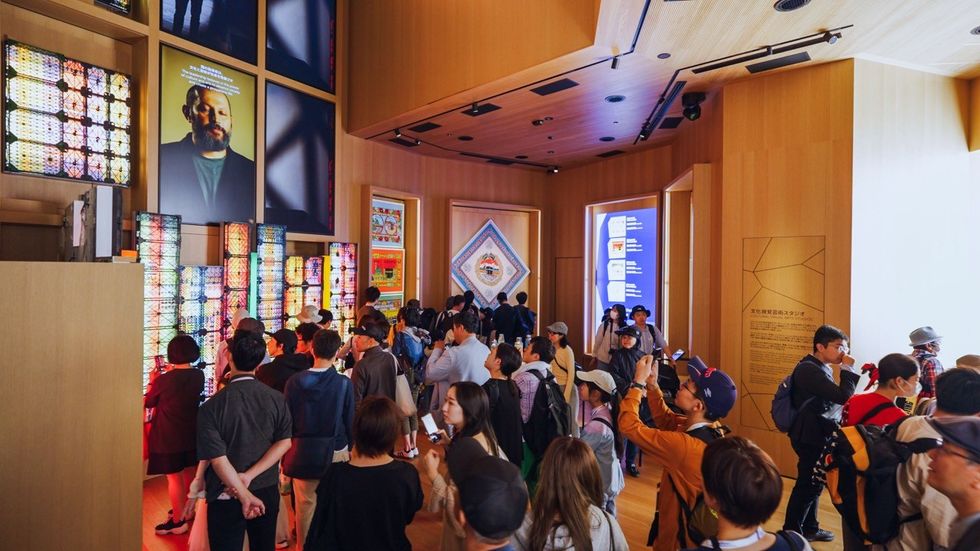 Crowded exhibition room with illuminated displays and digital portraits on the walls.