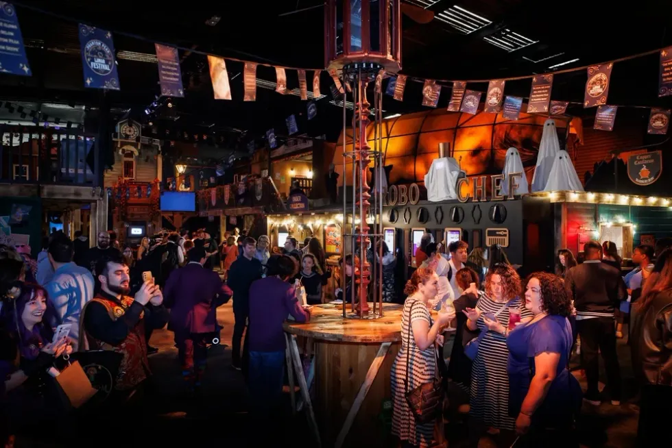 Crowded Halloween-themed indoor event with people socializing and taking photos.