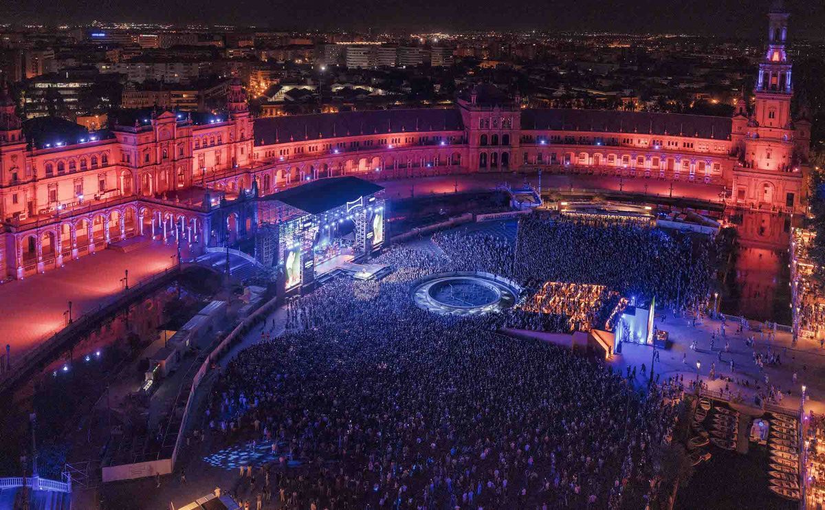 Crowded night concert at Plaza de España, Seville, with vibrant lighting and stage.