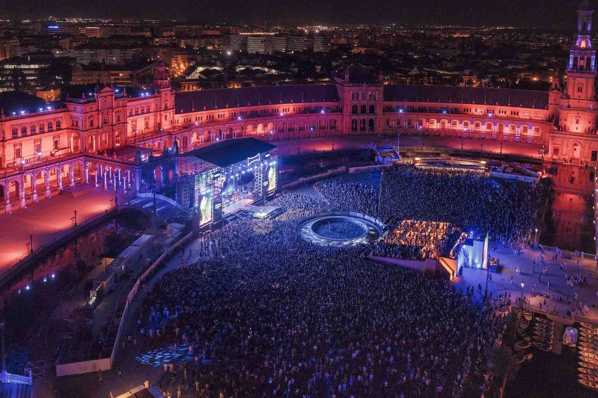 Crowded night concert at Plaza de España, Seville, with vibrant lighting and stage.