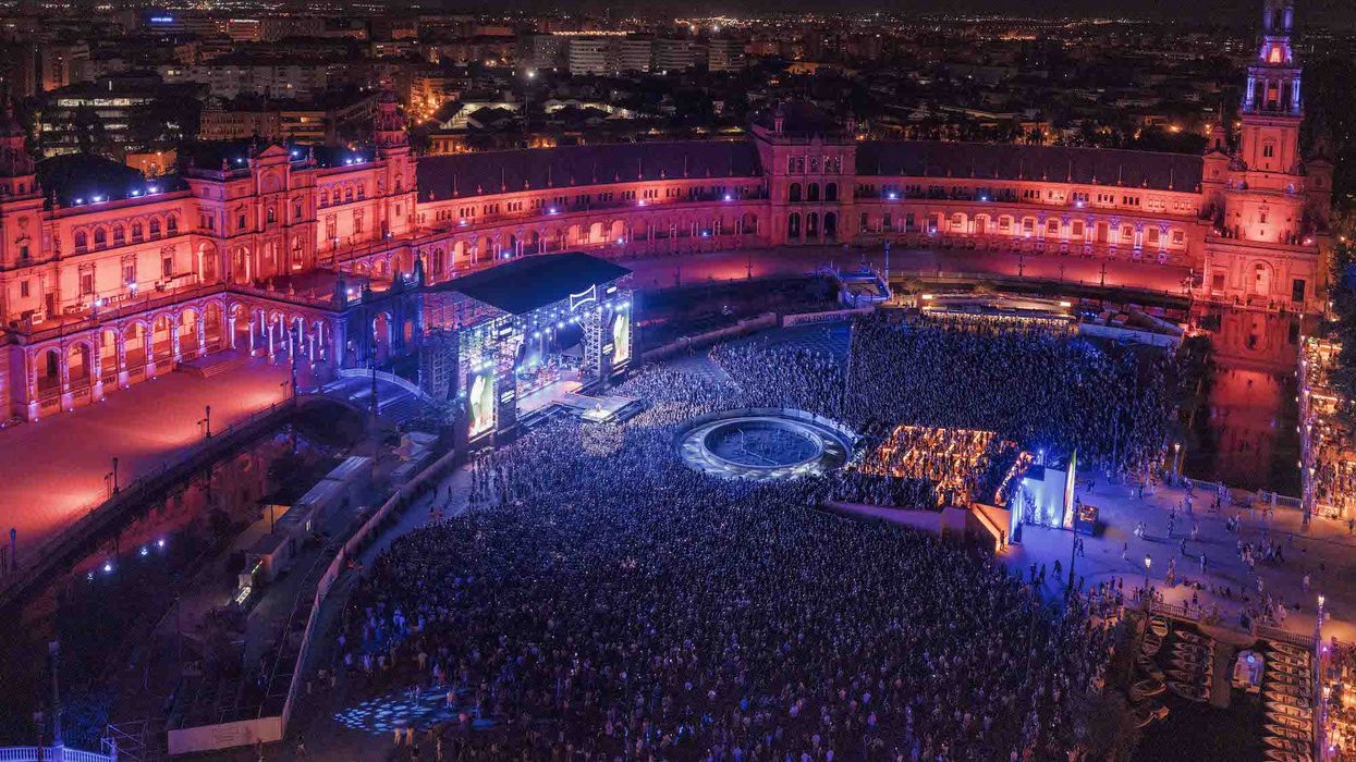 Crowded night concert at Plaza de España, Seville, with vibrant lighting and stage.