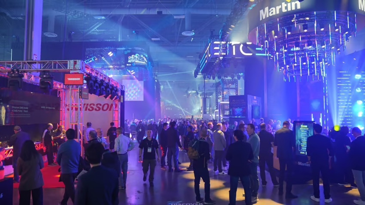 Crowded tech expo with vibrant blue and purple lighting and various booths.