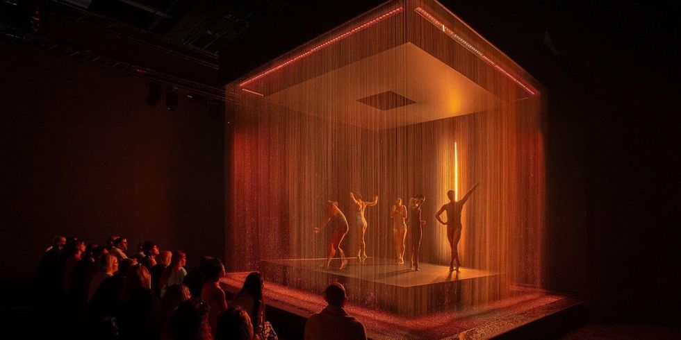 Crystal. Dancers perform under illuminated rain on a stage with an audience watching.