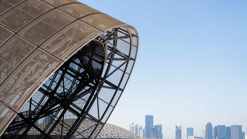 Curved modern architecture against a city skyline and clear blue sky.