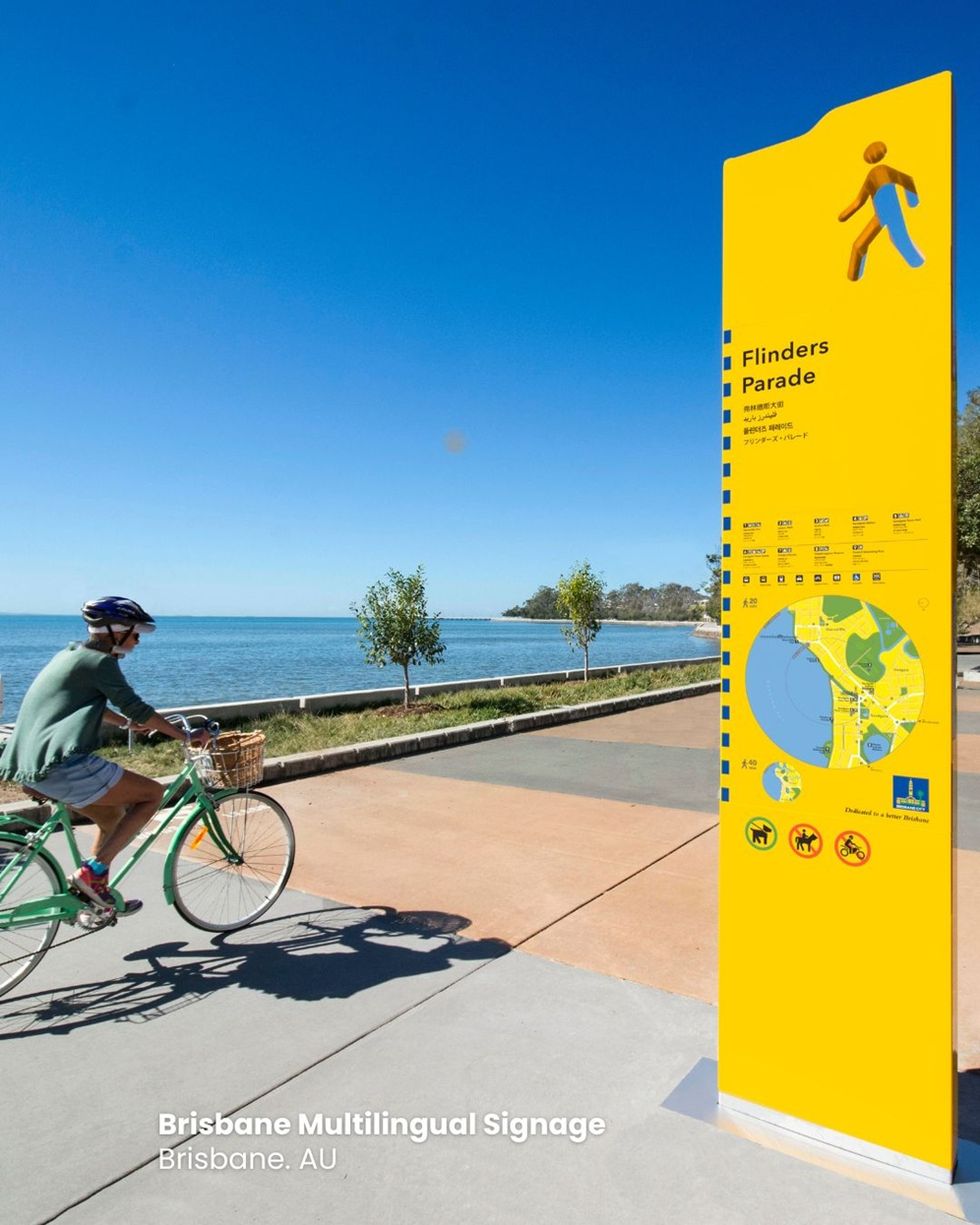 Cyclist passes bright yellow Flinders Parade sign by the seaside in Brisbane.