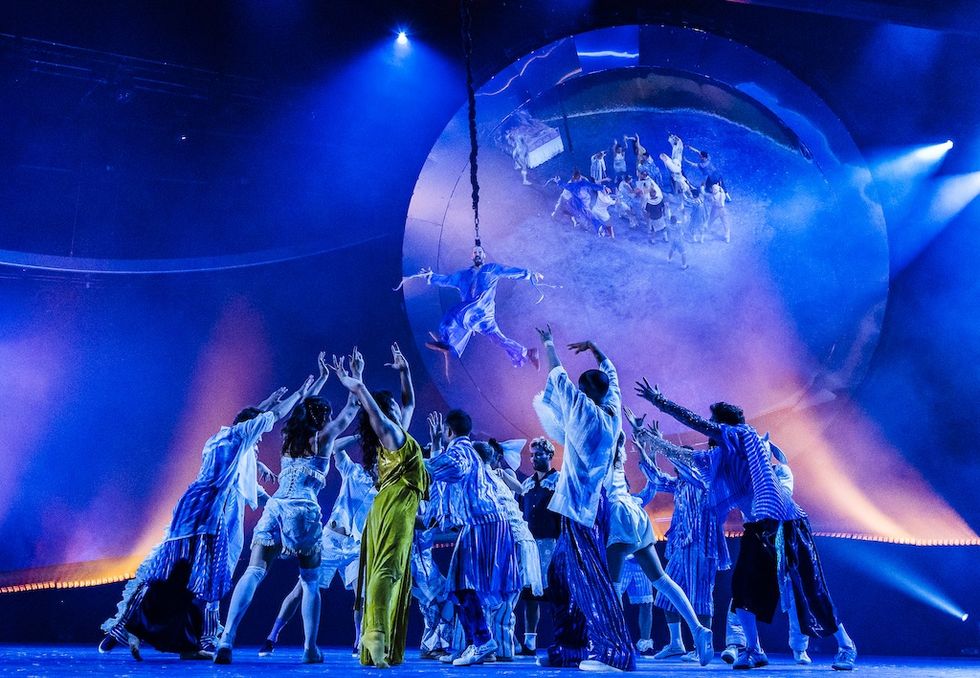 Dancers in vibrant costumes reach up to an aerial performer against a dramatic circular backdrop - Cirque du Soliel's LES INCOUCHABLES, Trois-Rivi\u00e8res