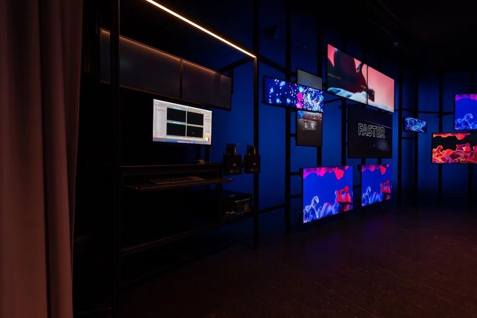 Dark room with multiple vibrant screens displaying digital art and the word "FASTER."