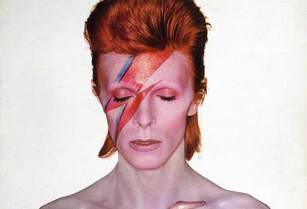 David Bowie with red hair and a painted lightning bolt across his face, eyes closed.
