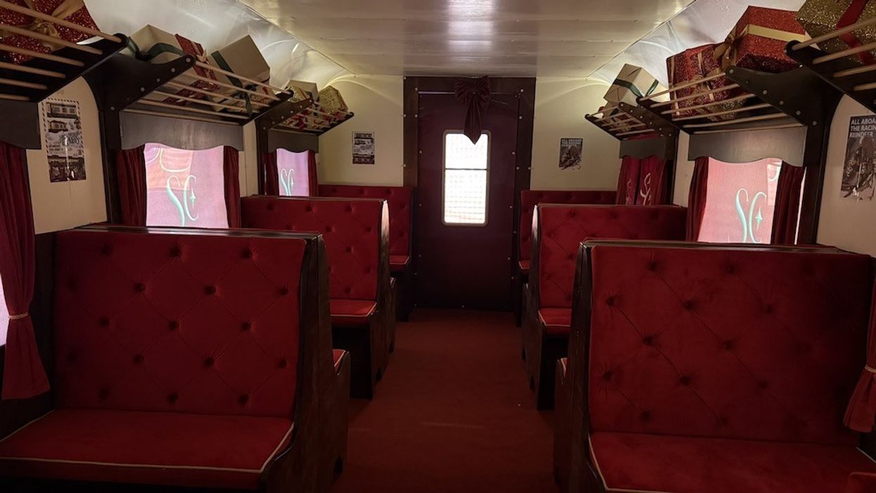 Decorated vintage train car interior with red velvet seats and gift boxes on shelves.