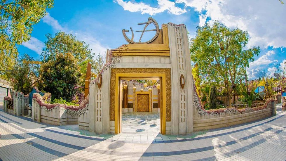 Decorative archway entrance at Disney California Adventure with gold details, surrounded by trees under a blue sky