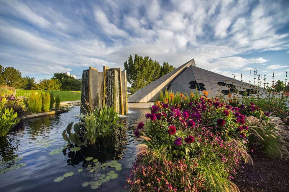 Denver Botanic Gardens with flowers, a modern pyramid structure, and a water feature under a cloudy sky.