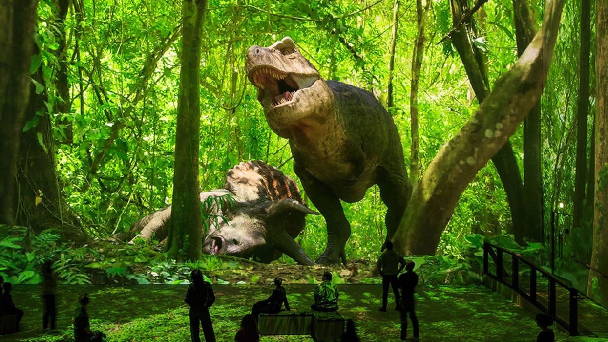 Digital T. rex and Triceratops in jungle, viewed by silhouetted museum visitors.