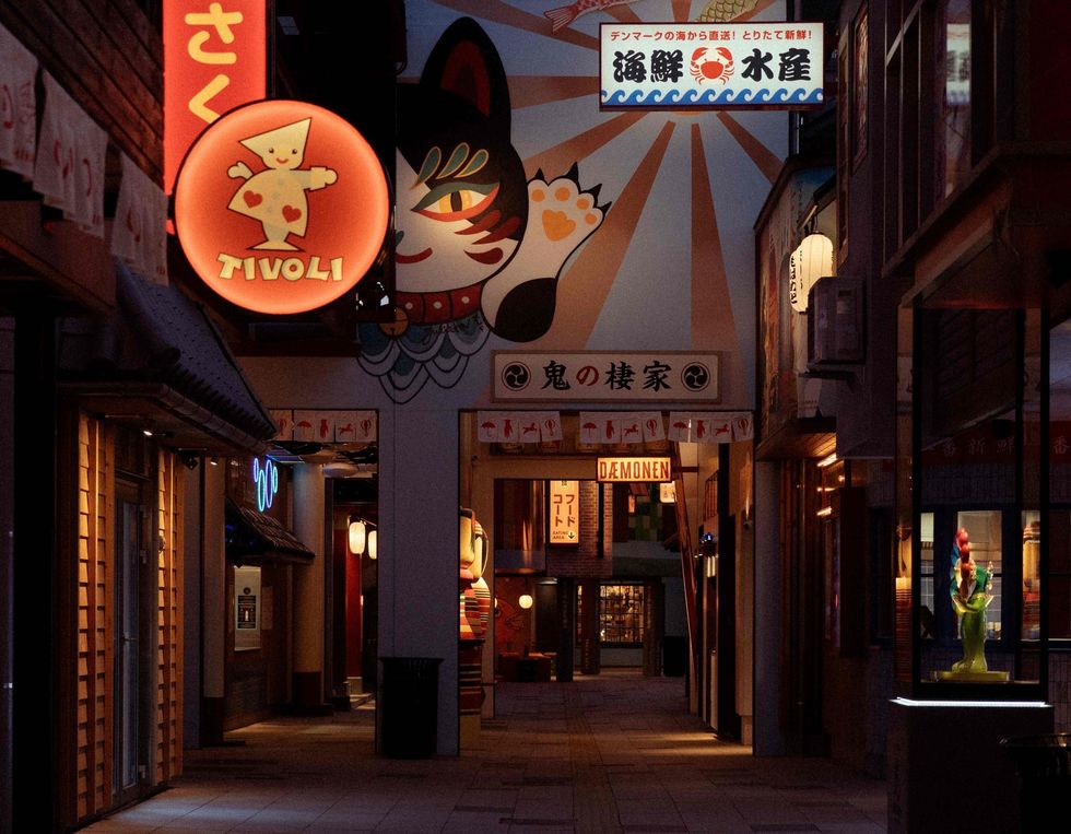 Dimly lit alley with vibrant neon signs and colorful murals at Tivoli Gardens