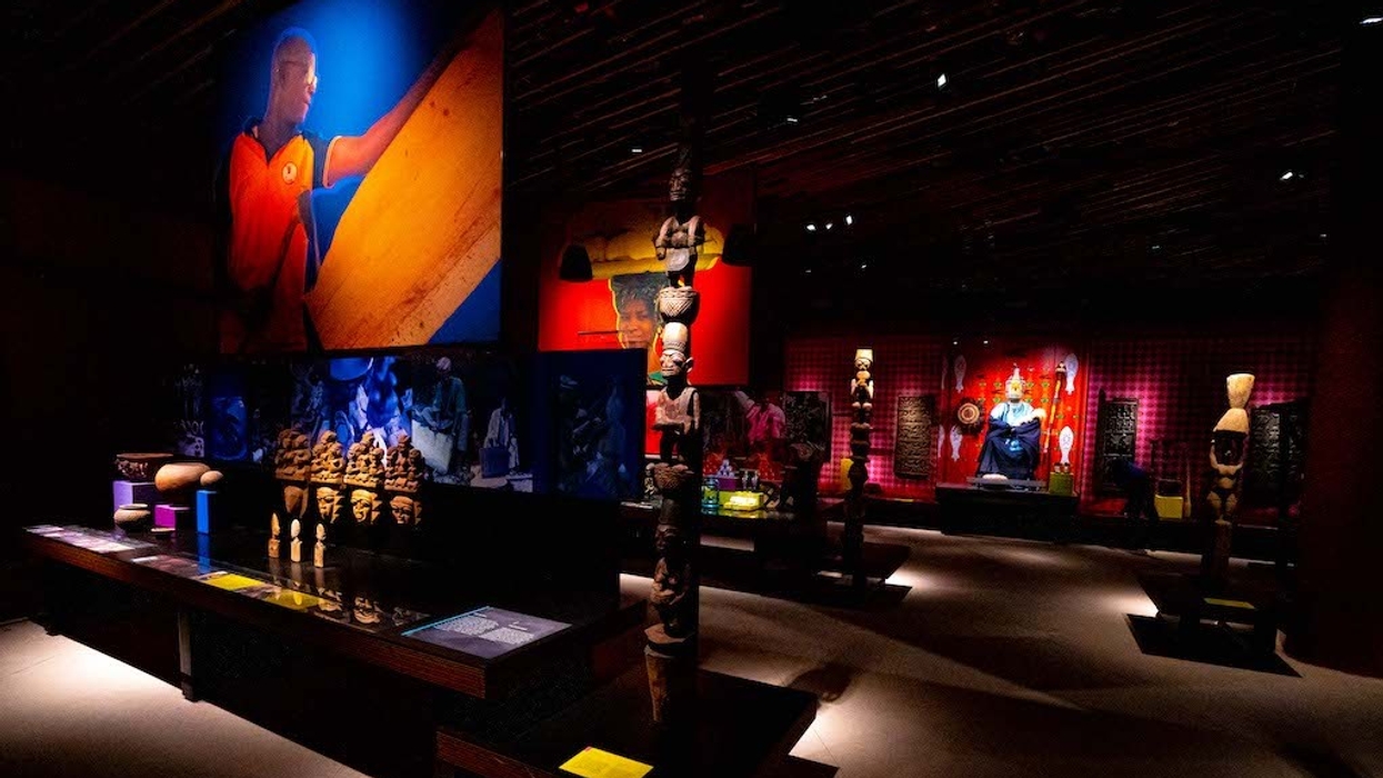 Dimly lit museum exhibit with African sculptures and large vibrant murals.