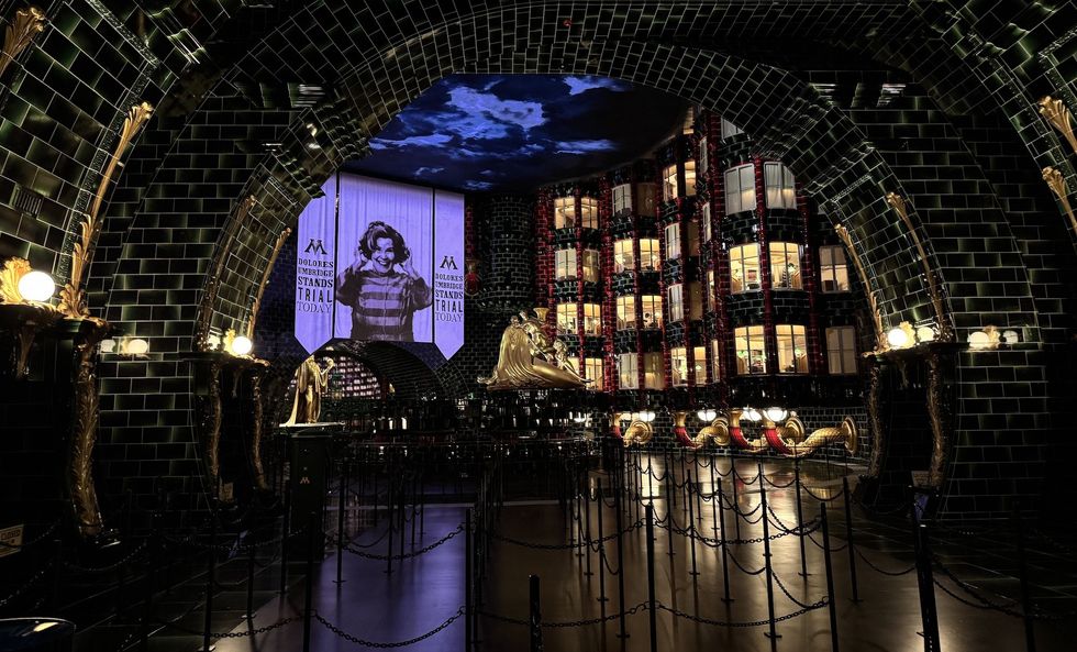 Dimly lit ornate hall with large display screen and chained queue lines, Harry Potter and the Battle at the Ministry