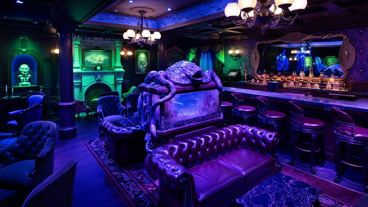 Dimly lit, ornate room with purple seating, decorative lighting, and a bar.