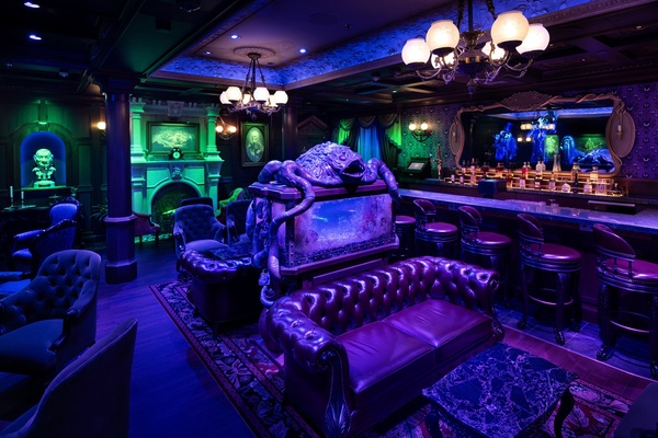 Dimly lit, ornate room with purple seating, decorative lighting, and a bar.