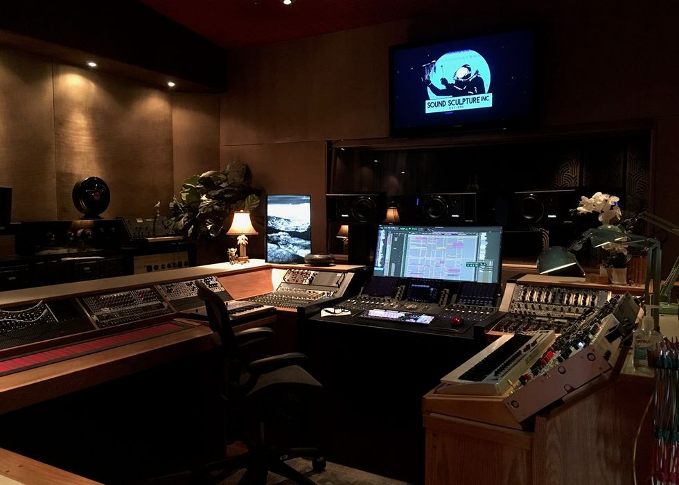 Dimly lit recording studio with mixing consoles and a computer screen.