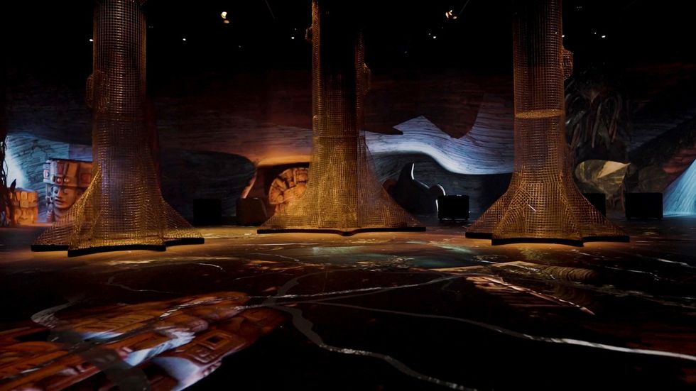 Dimly lit room in the Timewalk exhibition, with tall, illuminated lattice structures and colorful wall projections.