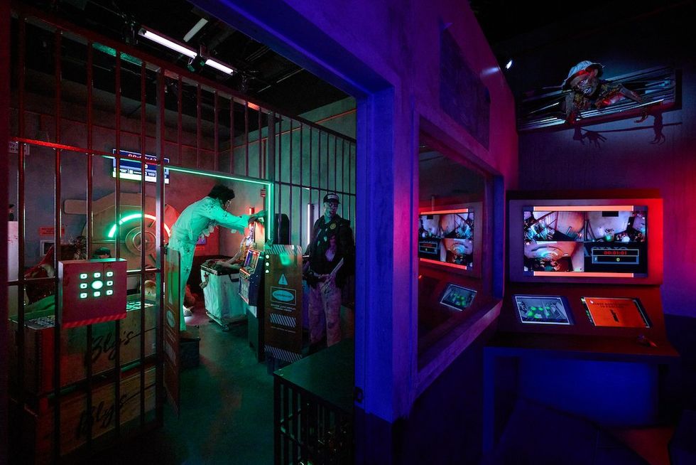 Dimly lit sci-fi lab with neon lights and monitors displaying surveillance footage.