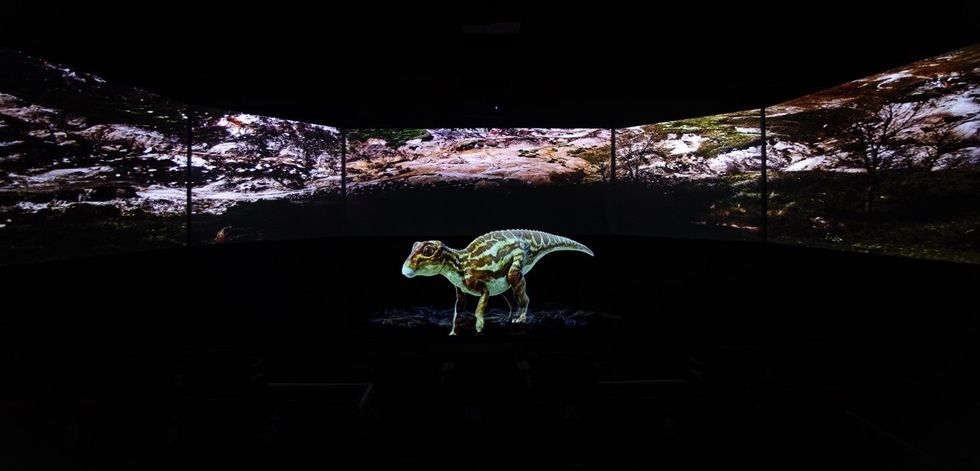 Dinosaur model in a dark room with panoramic landscape projection.