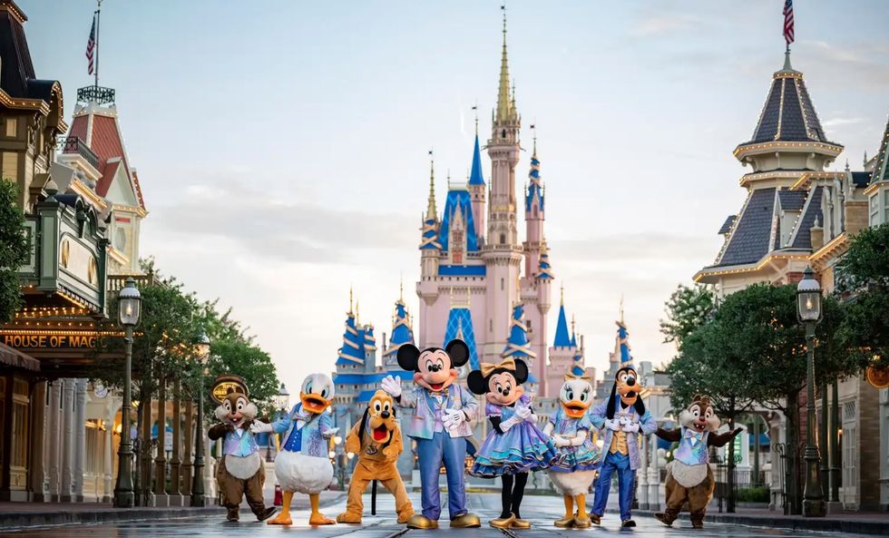 Disney characters pose in front of a castle on Main Street, with festive decorations.