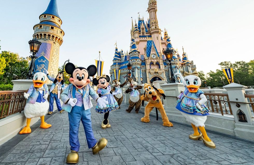 Disney characters pose in front of Cinderella Castle at a theme park.