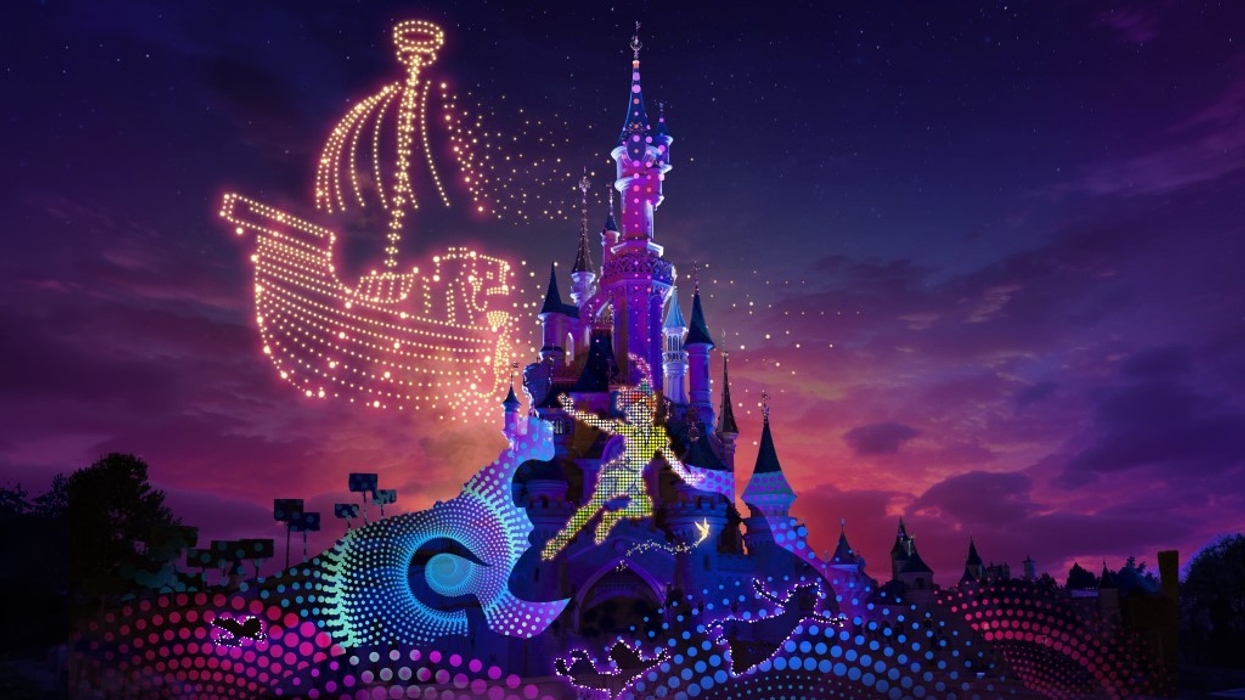 Disneyland Paris castle with colourful lights and projected Peter Pan at sunset, with drone show forming the shape of a ship