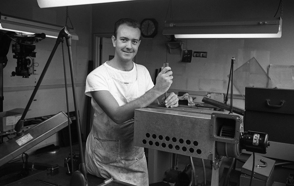 Don Iwerks smiling, working with machinery in a Disney workshop, wearing an apron.