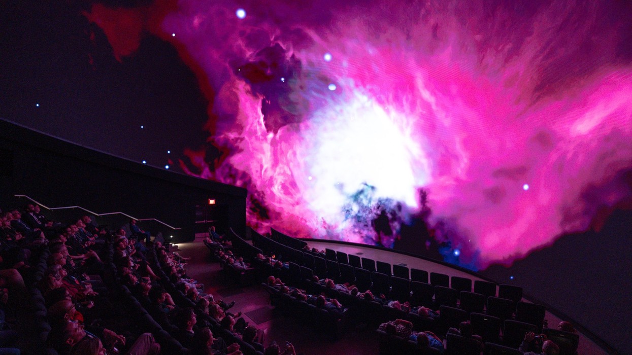 Dorrance DOME audience watching vibrant pink nebula projection on curved screen.