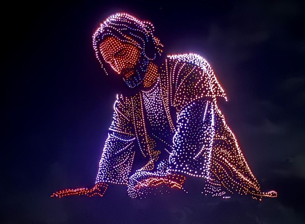 Drone light display from Aerial Illuminations forming a Jesus figure in colorful lights against the night sky.