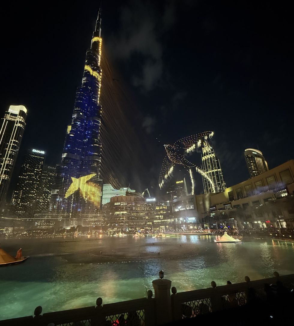 Dubai skyline at night with illuminated Burj Khalifa and colorful water fountain display.