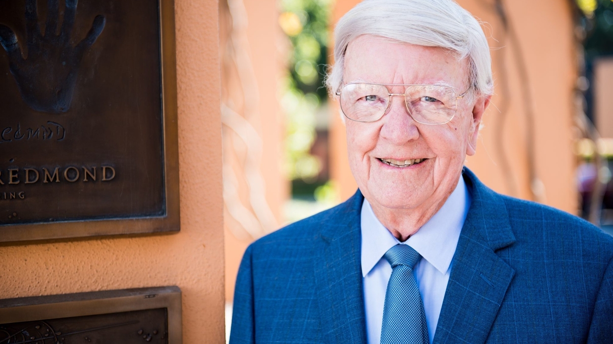 Elderly man called Don Iwerks in a suit smiling beside a plaque with a handprint.