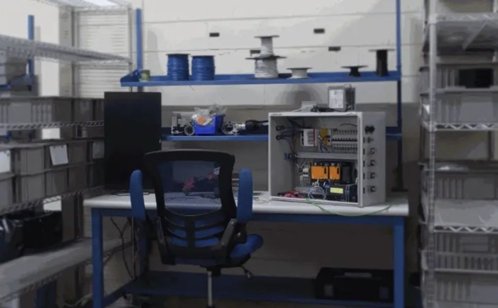 Electronics workstation at ProIO's new Florida facility, with a control panel on the desk and shelves of spools behind.